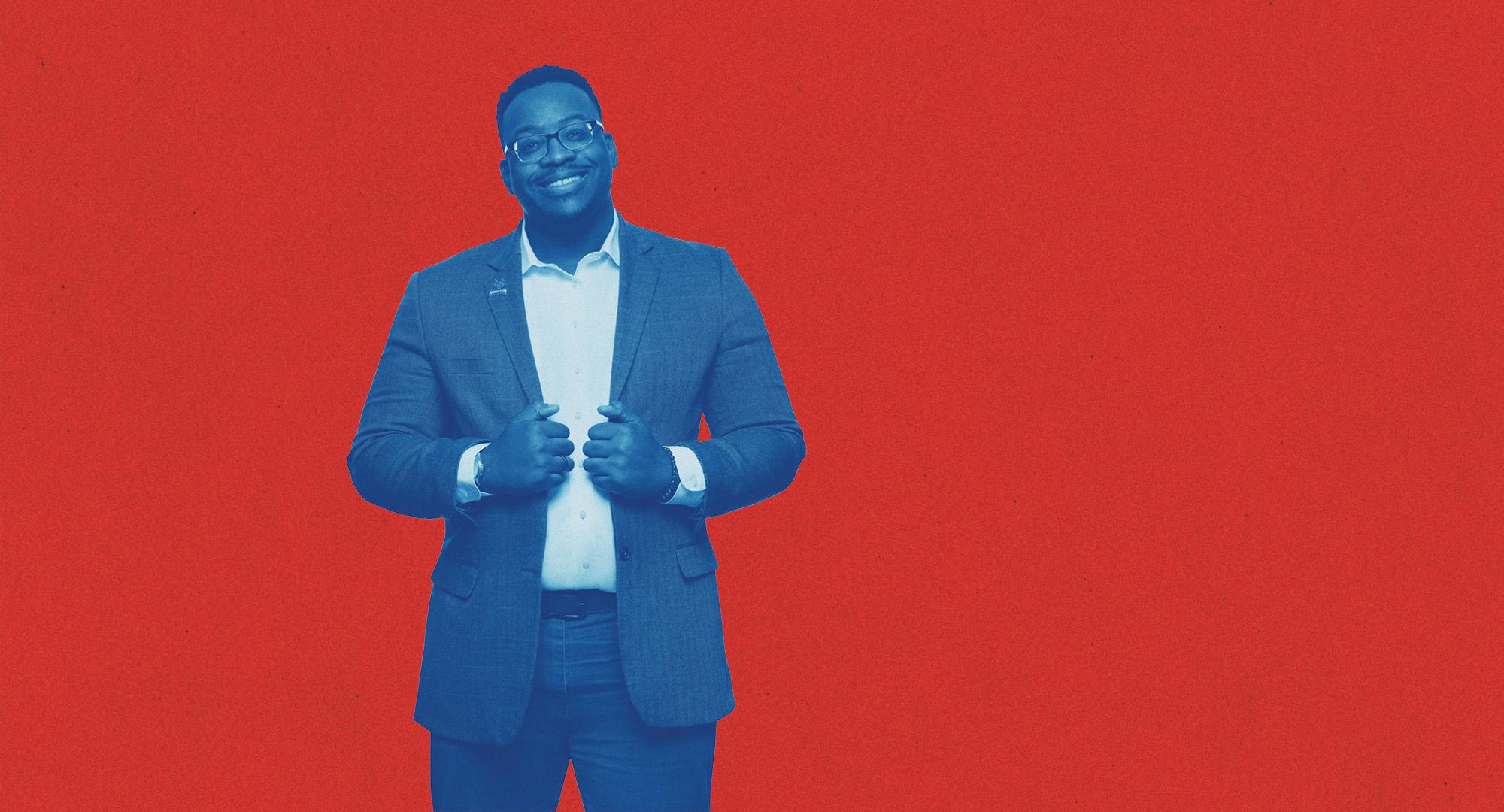 澳门新普京注册 Student dressed in a suit posing and smiling in front of a red background.